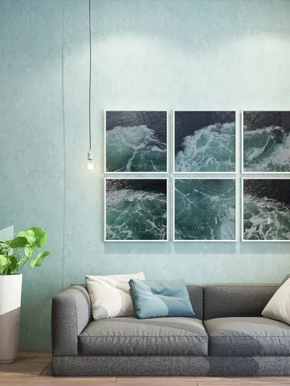 A simple yet effective living room design. The textured blue-gray wall, a comfortable gray sofa, and a gallery wall of ocean prints come together to create a calm, coastal-inspired vibe.
