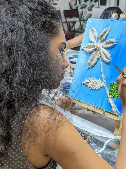 A close-up of a participant creating a textured flower on canvas. This technique involves building up layers of texture paste to create a 3D effect before painting.