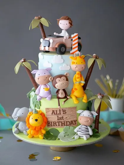 An amazing three-tiered jungle safari cake for a first birthday. This detailed creation features a whole crew of adorable fondant animals, including a lion, giraffe, monkey, and hippo.