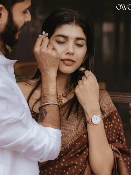 A close-up, tender moment as the groom-to-be gently places a flower behind his partner's ear during their traditional pre-wedding shoot.