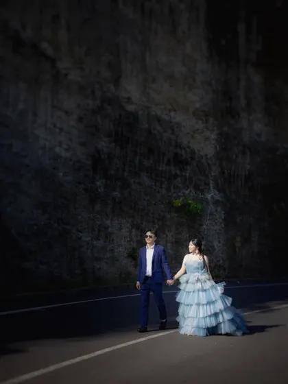 A full-length view of a couple walking together, showcasing their stylish outfits against a dark, textured cliffside. This is part of a series from a destination shoot in Bali.