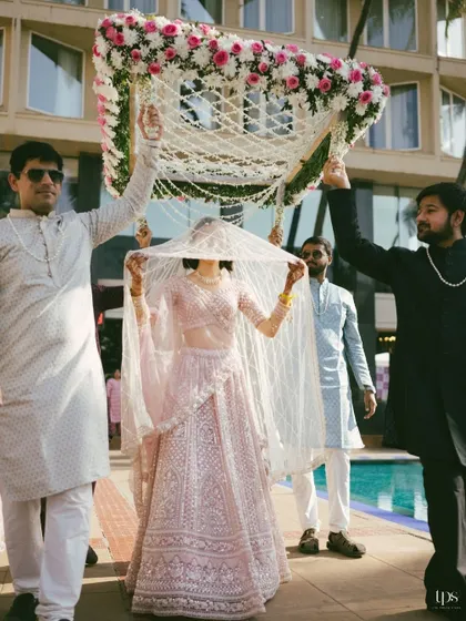 The bride's grand entrance under a delicate phoolon ki chadar. This shot captures the tradition and beauty of the bridal procession.