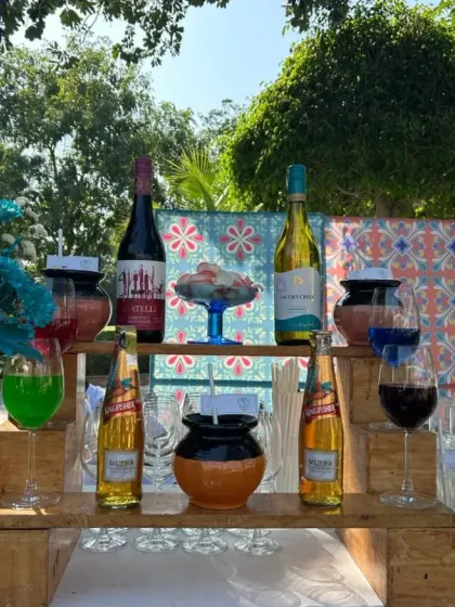 A colorful outdoor bar setup perfect for a daytime event. The display features a mix of wines, beers, and colorful cocktails, arranged on a rustic wooden pallet stand.