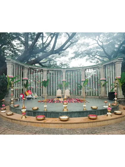 A breathtaking view of the wedding mandap at Shankaraa Foundation. The amphitheater-style seating is surrounded by traditional decor, including white chrysanthemums, pink nerium, and brass lamps, creating a sacred and harmonious atmosphere.