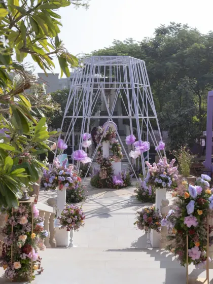 A large, white geometric structure at the entrance, adorned with lavender-hued floral clouds, creates a dramatic and modern welcome.