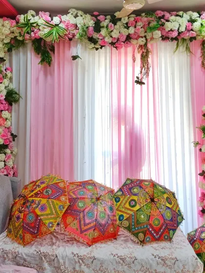 A beautiful baby welcome decoration for a home. I framed the living room area with pink and white flowers and placed decorative Rajasthani umbrellas on the sofa for a festive touch.