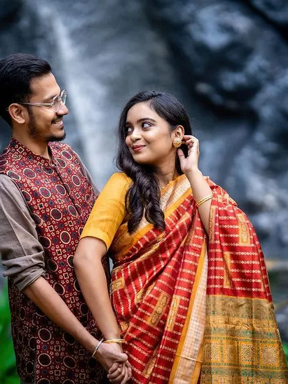 An elegant portrait of a couple in traditional attire, sharing a moment by a waterfall backdrop.