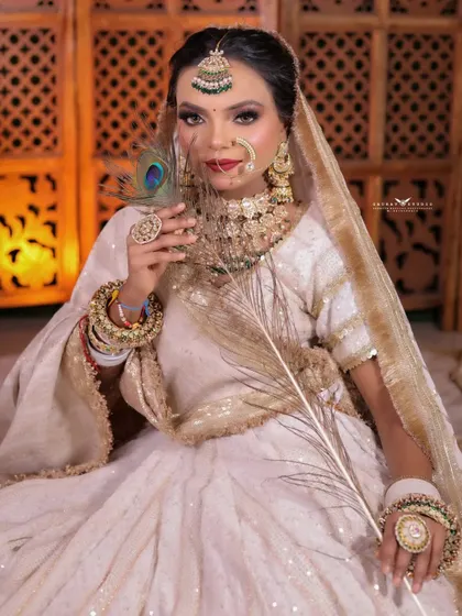 A full-length seated portrait where the bride holds a peacock feather. The prop adds a touch of traditional symbolism and artistry to the modern white lehenga.