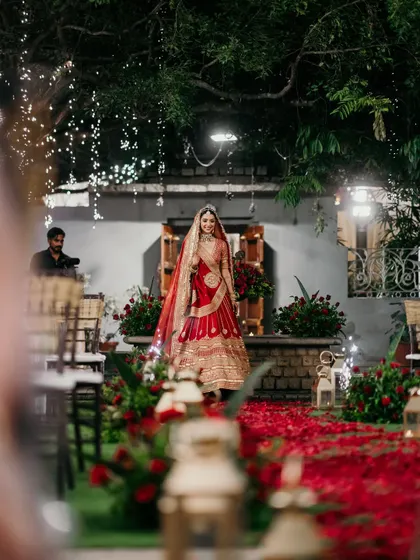 The bride's grand entrance on an aisle of red rose petals. We believe the bridal entry should be a show-stopping moment, and we design every detail, from the lighting to the floral path, to make it unforgettable.