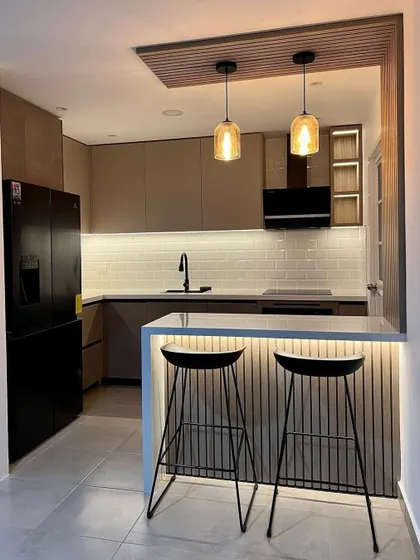 A compact L-shaped kitchen with a minimalist breakfast bar for two. The use of fluted panels and pendant lights adds a touch of modern elegance to the small space.