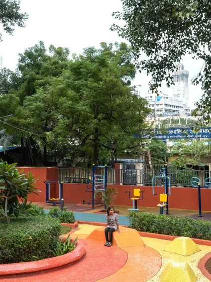 A child sits on a colorful planter edge in the VDP Garden play area. The design uses varied heights and colors to create an engaging and imaginative landscape for children.