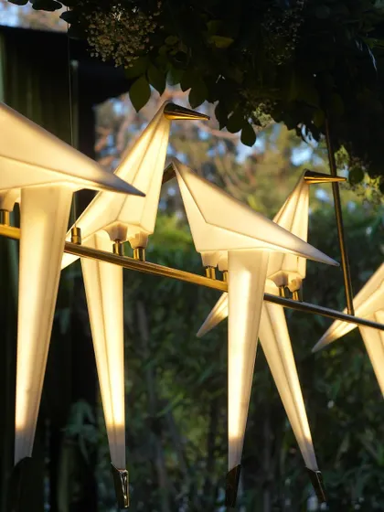 Unique, illuminated origami bird lights are perched on a branch, adding a touch of modern artistry and soft light to the space.