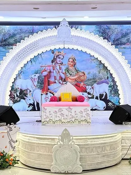 The main stage for a seven-day Bhagwat Sapta event at Hiravati Hall. We created a serene all-white setup with an ornate arch framing a Radha-Krishna backdrop, complemented by decorative sun-like motifs and Pichwai cows.