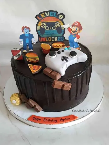 Game on! This gaming themed cake is perfect for an 8th birthday, featuring a controller, characters from Mario and Roblox, and edible junk food snacks.
