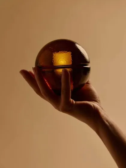 A hand holds the sepia-colored Bocci 14p, giving a sense of its satisfying, palm-sized form and portability.