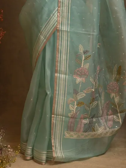 A dreamy blue organza saree with hand-embroidered florals on the pallu and delicate mirror work all over.
