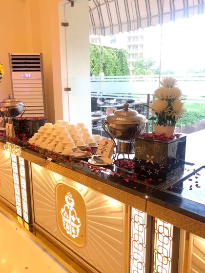 An elegant dessert and beverage counter from a recent event. The illuminated facade with a royal crest design, black marble top, and scattered rose petals creates a sophisticated and inviting display.