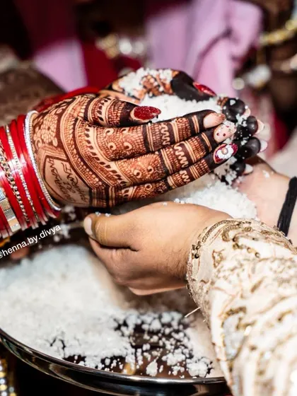 A candid shot from a wedding ceremony, showing the bride's hands with a deep henna stain during a ritual. The color is rich and prominent.