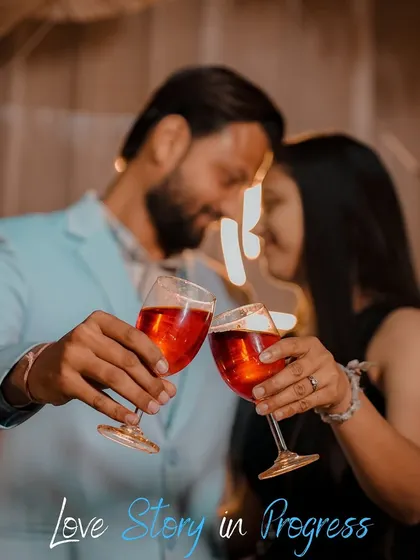 A soft-focus shot of a couple sharing a toast, capturing a celebratory and intimate moment. The "Love Story in Progress" text adds a sweet narrative touch.