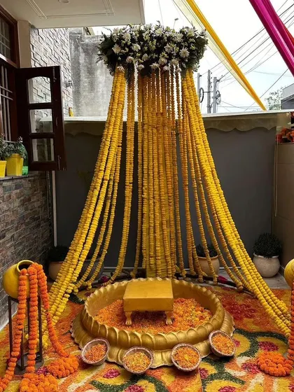 A stunning Haldi ceremony setup featuring a canopy of cascading marigold strings. The central 'urli' is surrounded by marigold petals and garlands, creating a traditional and immersive experience.