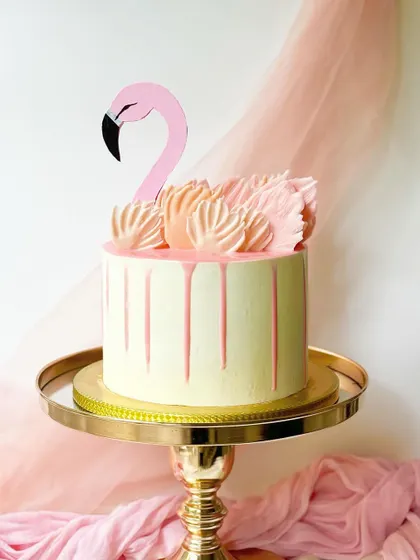 A fun and tropical flamingo cake. This design features a pink drip, piped buttercream "feathers," and a flamingo topper.