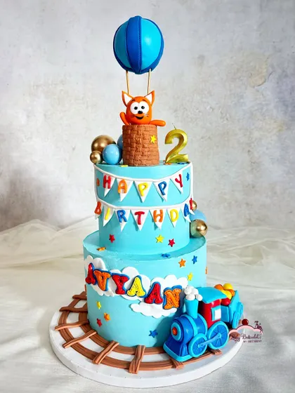 A fun and imaginative two-tier cake for a boy who loves trains and hot air balloons. The colorful bunting and stars add to the celebratory feel.