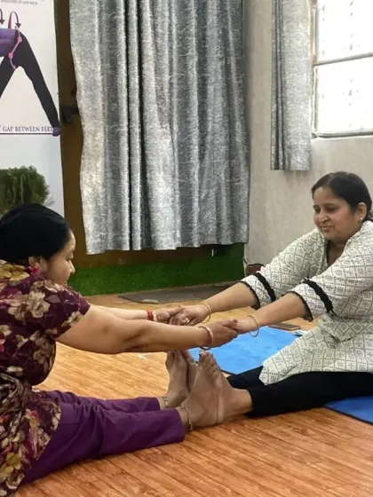 Partner work helps deepen stretches safely. Here, two students assist each other in a seated forward bend (Paschimottanasana), using gentle resistance to increase hamstring and back flexibility.