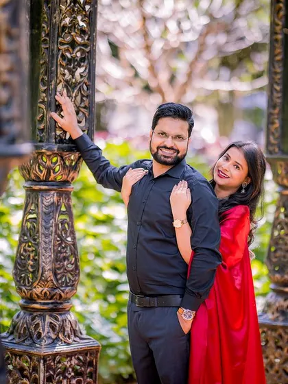 A stylish portrait of a couple in a corridor of pillars. The bride's red saree and the groom's black shirt create a bold and modern look.