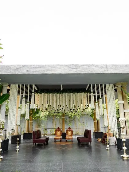 A stunning wedding mandap at Prangana Venue, adorned with lush white chrysanthemums and fragrant tuberoses. The design is elevated with golden bells, metal urli pots, and banana leaves, creating a perfect blend of heritage and beauty.