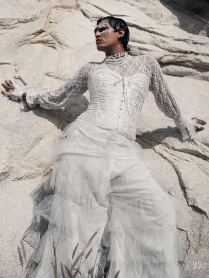 The all-white ensemble and makeup stand out beautifully against the textured rock face.