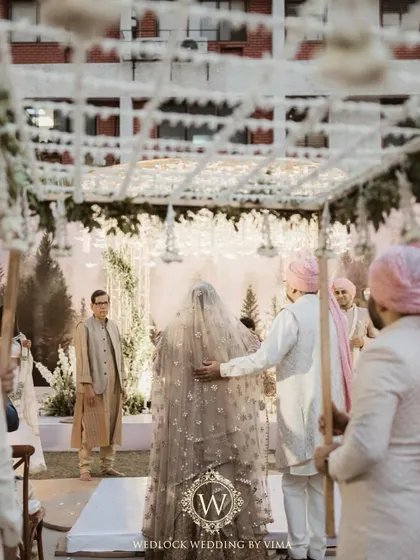 The bride's grand entrance under a beautiful phoolon ki chadar made of fresh white flowers and greenery. This moment was part of a minimalist wedding with an elegant white and green theme.