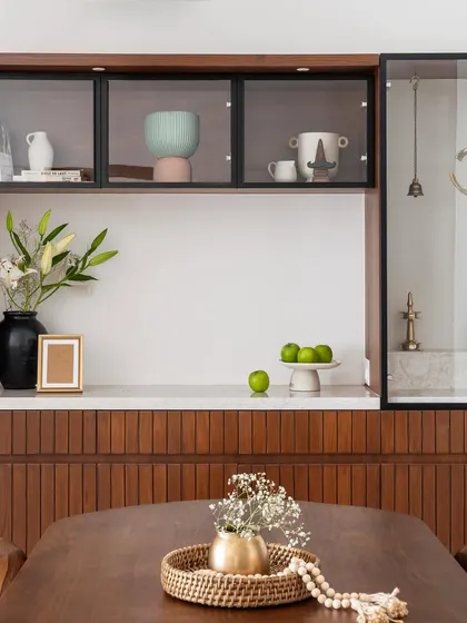 A low-height crockery unit that also incorporates a puja space, featuring fluted wood paneling and glass display cabinets.