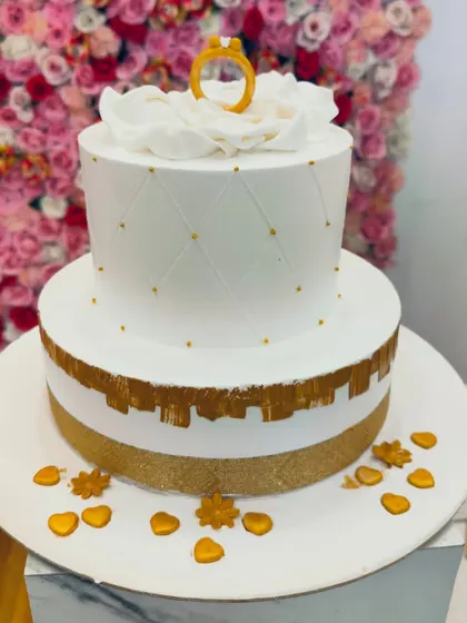 A beautiful two-tiered engagement cake with a white quilted pattern and gold accents. The single ring on top is a simple and elegant touch.