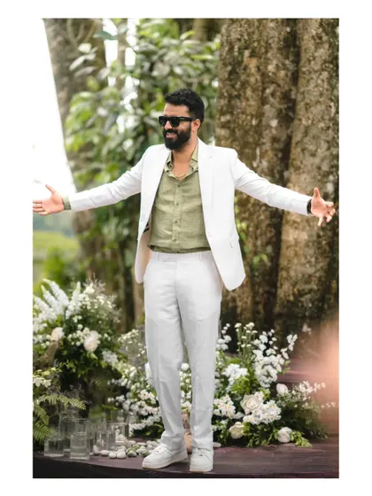 A groom with his arms wide open, embracing the joy of his wedding day. His confident and happy expression is infectious, captured in a beautiful outdoor setting.