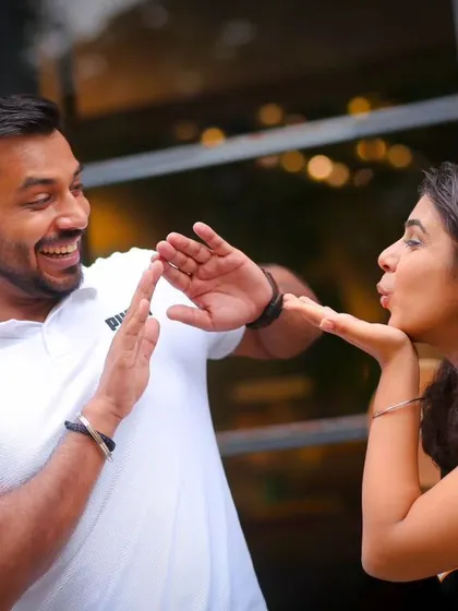 A playful interaction during a pre-wedding shoot. The bride-to-be blows a kiss to her partner, who reacts with a fun, defensive pose, capturing their dynamic and joyful relationship.
