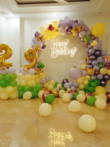A vibrant and fun balloon arch for a 29th birthday. I used a mix of purple, green, yellow, and metallic balloons, with butterfly accents and a neon sign to create a cheerful photo corner.