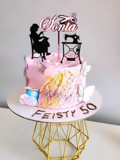 A custom acrylic topper for a 50th birthday with a sewing theme. The design features a silhouette of a woman sewing, a vintage machine, and the personalized name.