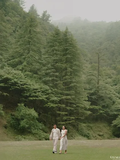 A wide shot of the couple walking hand-in-hand through a misty forest in Mussoorie, creating a moody and romantic atmosphere.