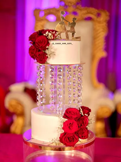 Our popular crystal chandelier wedding cake, beautifully lit against a vibrant pink background. The fresh red roses add a classic touch of romance.