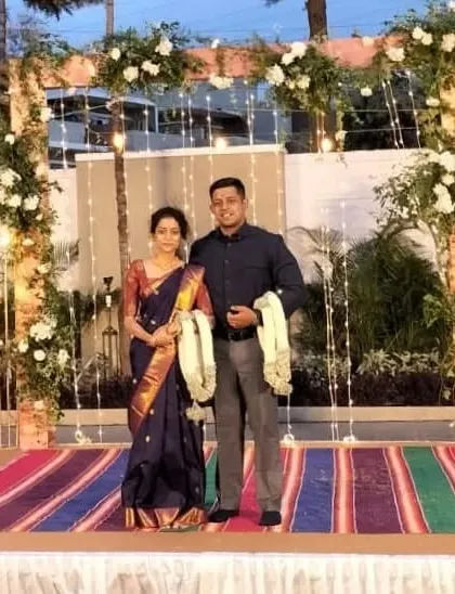 A lovely couple poses for a photo under a floral arch decorated with white roses and fairy lights, a perfect example of a simple yet beautiful photo opportunity we can create.