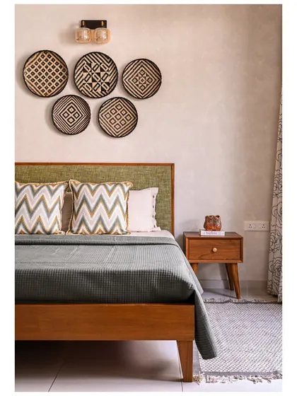 An earthy bedroom with a khadi green upholstered headboard, woven wall baskets, and textured walls for a serene, welcoming feel.