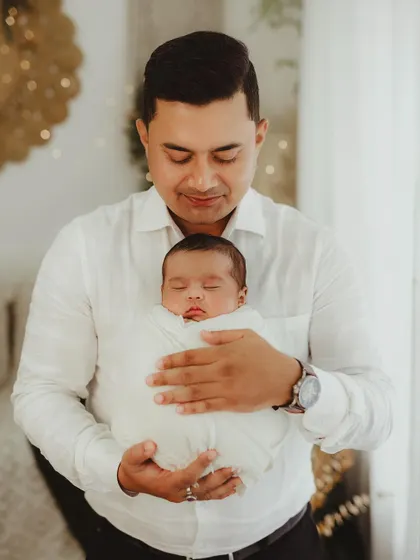 A father gently holds his swaddled newborn, a portrait of quiet strength and tenderness.