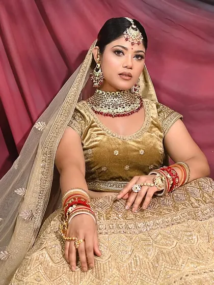 A full-length portrait showcasing the elegance of the golden lehenga against a dramatic red and black backdrop.