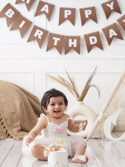 A happy baby girl enjoys her first birthday cake in a boho-themed setup, complete with a miniature tent and a 'One' sign.