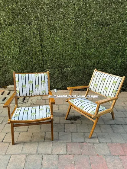 A pair of light-framed wooden chairs with a playful, striped fabric featuring a palm tree motif.
