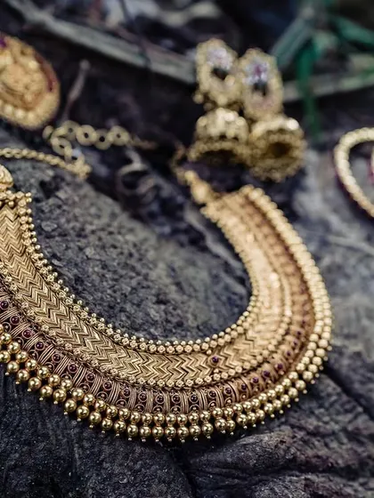 An artistic flat lay of the bride's temple jewelry on a piece of textured wood. This shot highlights the intricate craftsmanship of the traditional gold necklace, earrings, and bangles.