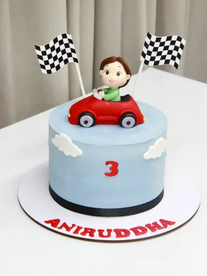 A cute and simple car-themed cake for Aniruddha's 3rd birthday, featuring a little driver in his red convertible, ready to race.