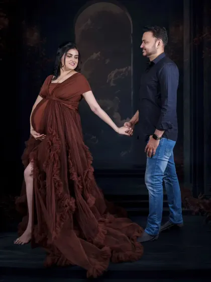 A dramatic and romantic pose against a dark, moody backdrop. The couple holds hands, with the flowing brown gown adding a touch of elegance and movement to the scene.