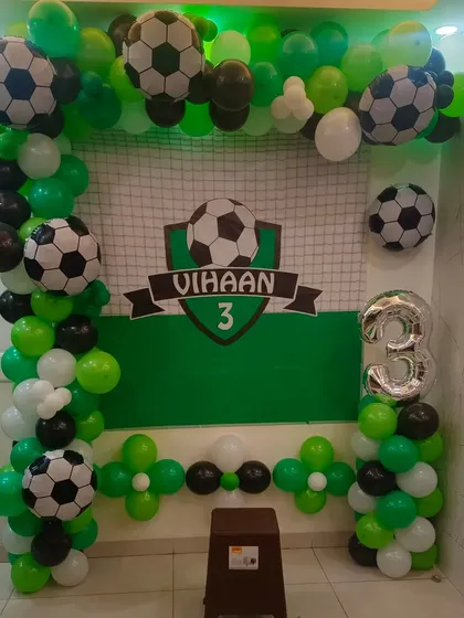 A football-themed 3rd birthday decoration set up in a home, featuring a custom backdrop and a green, black, and white balloon arch.