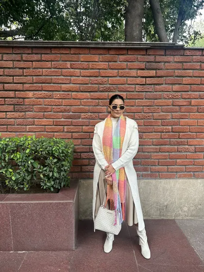 A chic winter outfit featuring a cream-colored dress and long cardigan, white boots, and a colorful pastel scarf for a pop of color.